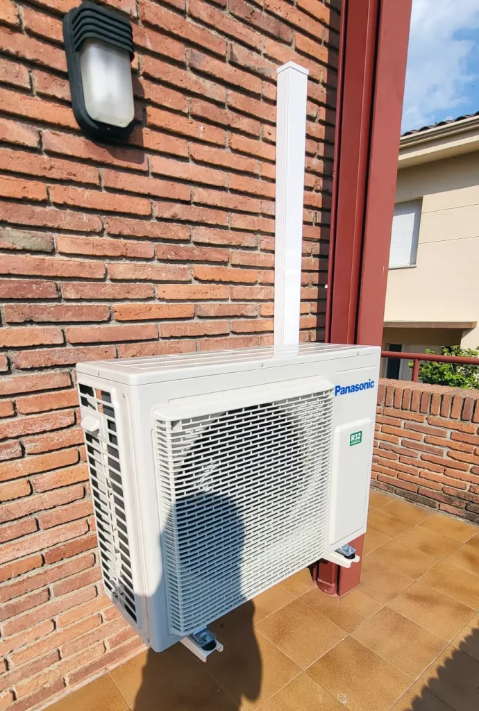 Unidad exterior de aire acondicionado instalada en una fachada de ladrillo.