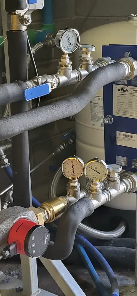 Detalle de intercambiador de calor con válvulas y manómetros en sistema de climatización.